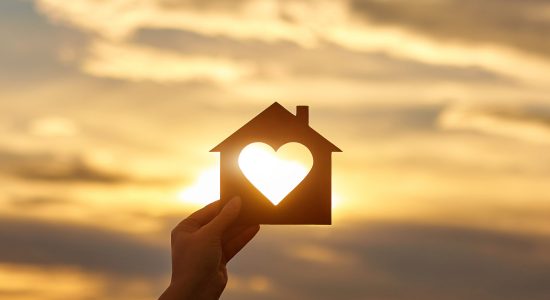 Woman hand holds wooden house in the form of heart against the sun Woman hand holds wooden house in the form of heart against the sun. Solar energy. Children dreams. International day of families. Home protection insurance concept. Planning to buy property. A symbol for ecology.